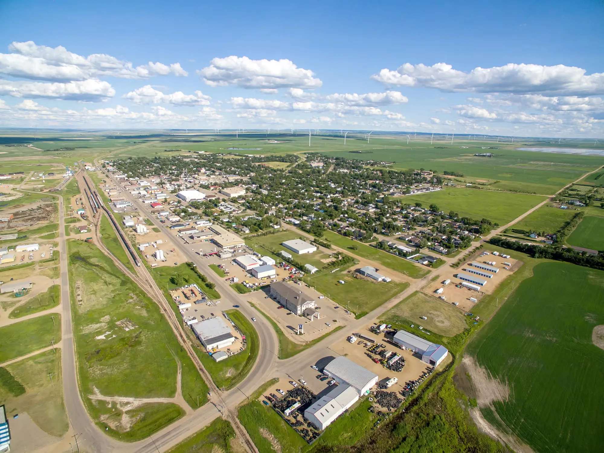 Aerial view of Assiniboia, Saskatchewan — the rail line through town and the Potentia wind farm turbines on the horizon